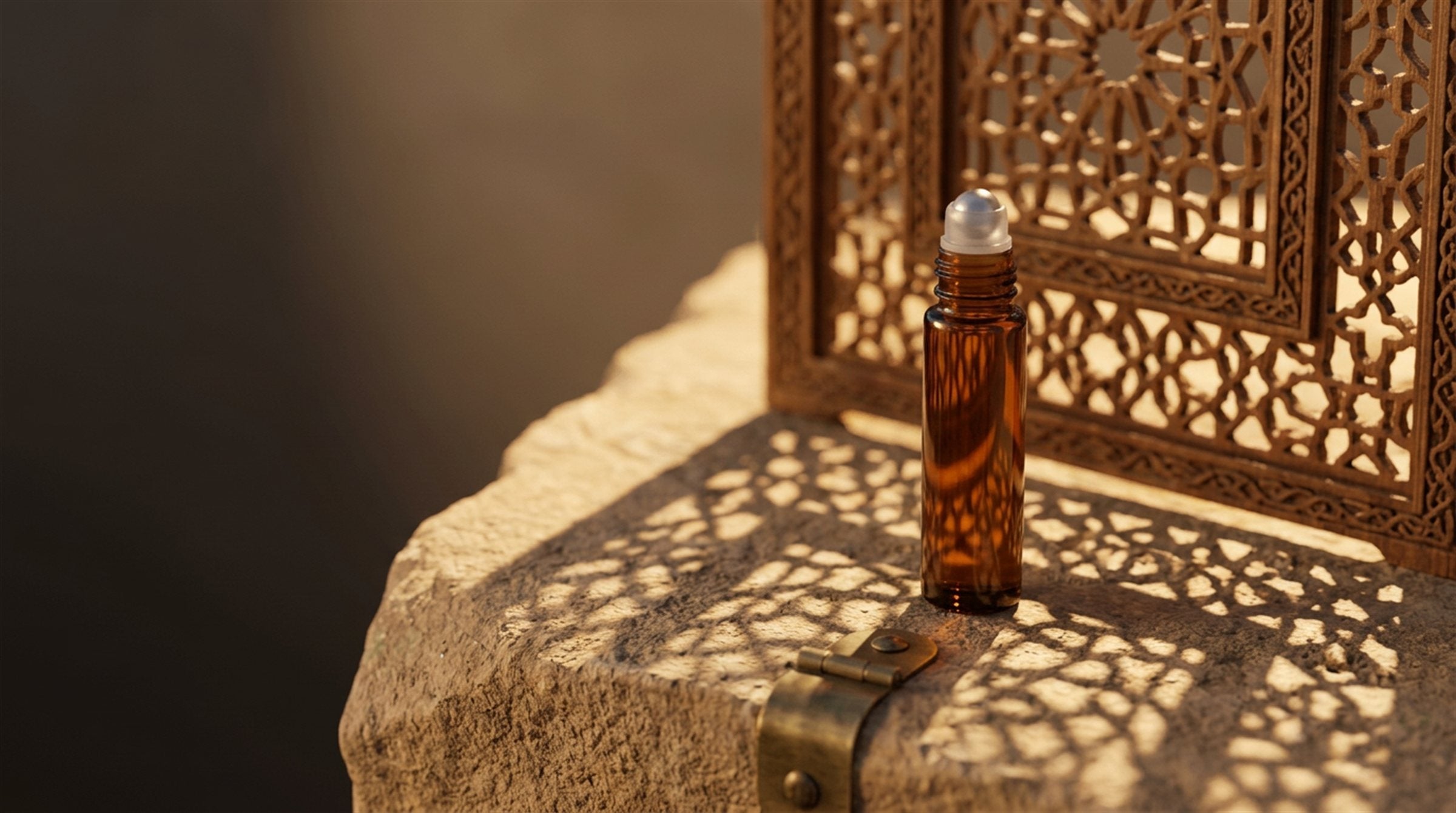 A 20.O2 amber glass roll-on oil vial on warm stone, with the geometric shadow of a carved mashrabiya screen falling across it