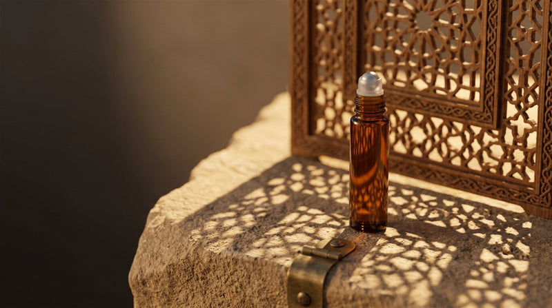 A 20.O2 amber glass roll-on oil vial on warm stone, with the geometric shadow of a carved mashrabiya screen falling across it